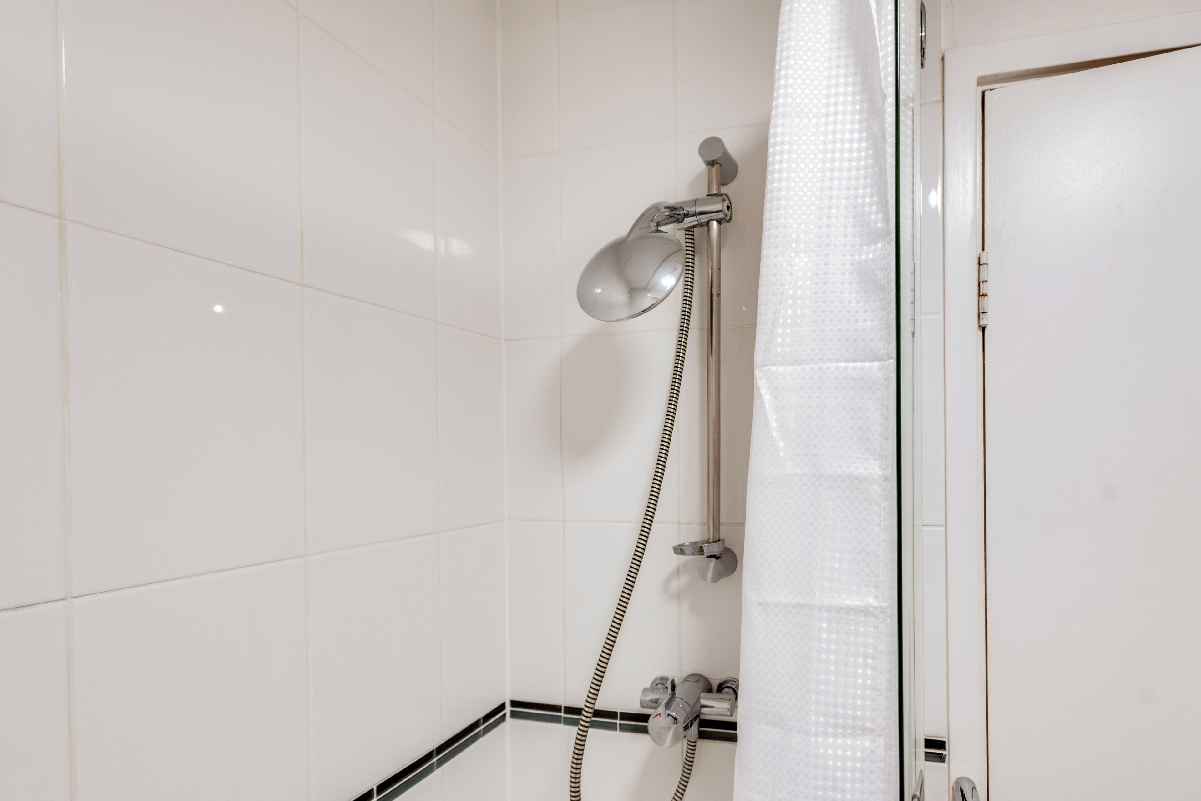 A bathroom with white tiled walls, a shower with a handheld showerhead, and a towel rack.