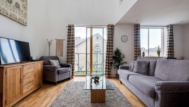 Ein modernes Wohnzimmer mit grauem Sofa, Holzschrank und Glastisch.
