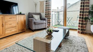 Ein modernes Wohnzimmer mit einem Glastisch, einem grauen Sofa, Holzschränken und Blick ins Freie.