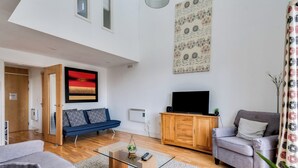 Ein modernes Wohnzimmer mit einer Couch, einem Sessel und einem Fernseher auf einer Holzkommode.