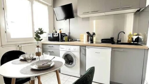 A compact kitchen with a washing machine, a sink, and a flat-screen TV mounted above it. - Studio Lumière du Centre - Parking - Romans (Romans-sur-Isère)