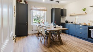 Une cuisine moderne avec une table à manger pour quatre personnes, des meubles de rangement aux couleurs sombres et une fenêtre donnant sur un paysage verdoyant.
