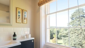 Une salle de bain avec un lavabo blanc, des meubles noirs, une fenêtre donnant sur les arbres et deux tableaux encadrés accrochés au mur.
