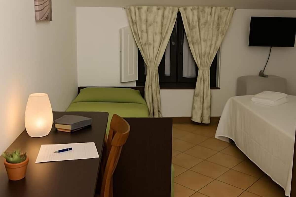 A hotel room with a bed, a desk with a lamp, a chair, a TV, and a window with curtains.