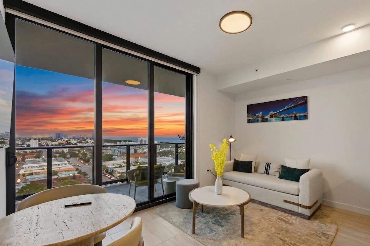 A modern living room with a large window, a sofa, a coffee table, and a painting on the wall.