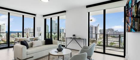 Uma sala de estar moderna com sofá, cadeiras, mesa de centro e uma grande janela com vista para a cidade.