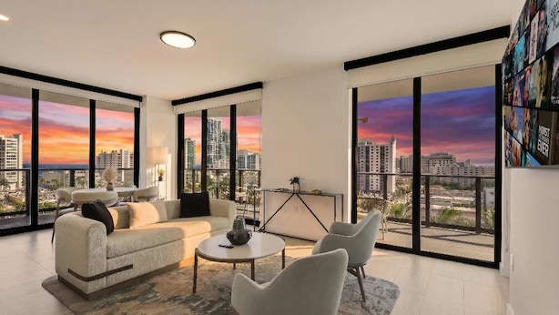 A modern living room with a city view, a sofa, a coffee table, and a bookshelf. - Elegant Miami Beach Condos (Miami Beach)