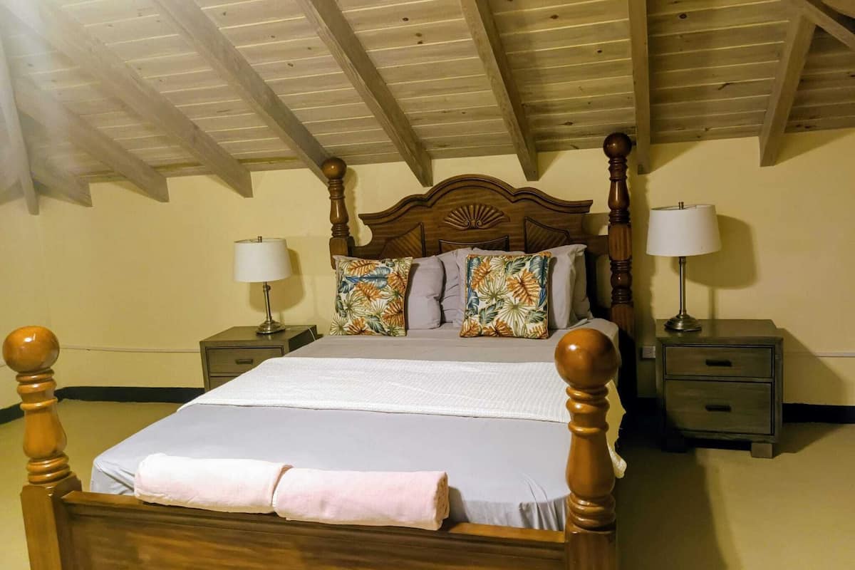 A wooden four-poster bed with a headboard, two bedside tables with lamps, and floral-patterned pillows.