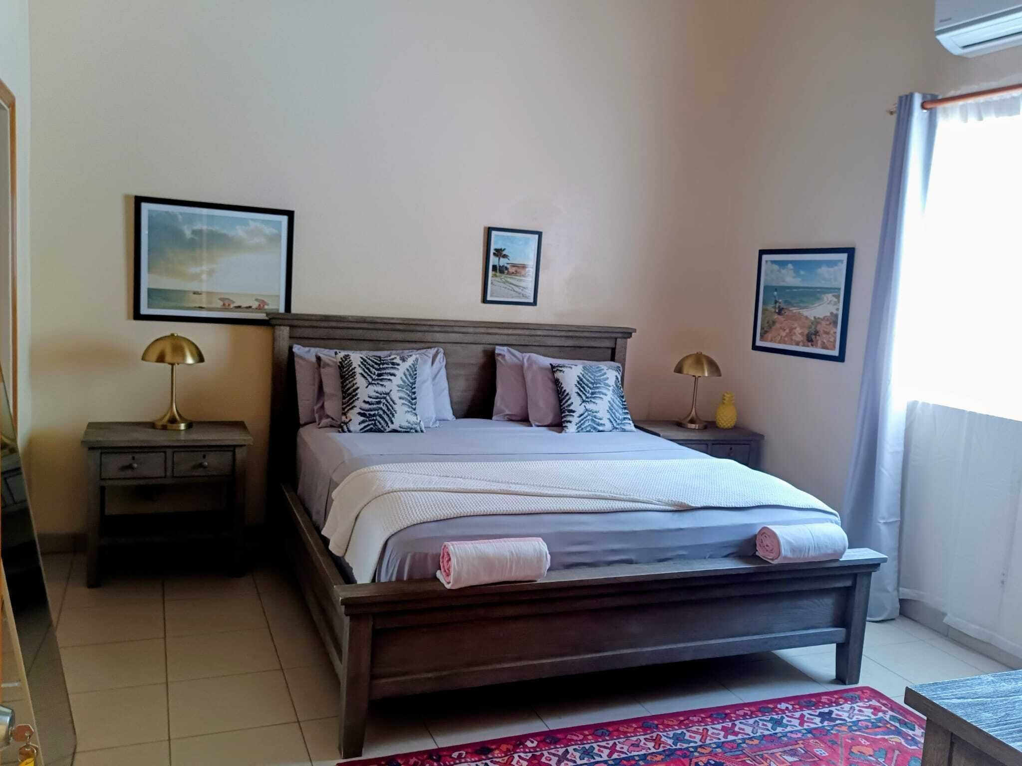 A bedroom with a wooden bed, two bedside tables with lamps, a patterned rug, and two framed pictures on the wall.