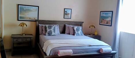 A bedroom with a wooden bed, two bedside tables with lamps, a patterned rug, and two framed pictures on the wall.
