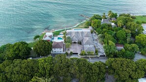 Vista aérea de una propiedad costera con piscina, varias edificaciones y abundante vegetación.