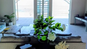 A living room with a sofa, a coffee table, and a potted plant. There is a view of the beach through the open doors. - Turtle Cove House by Le Haus (St. John's)