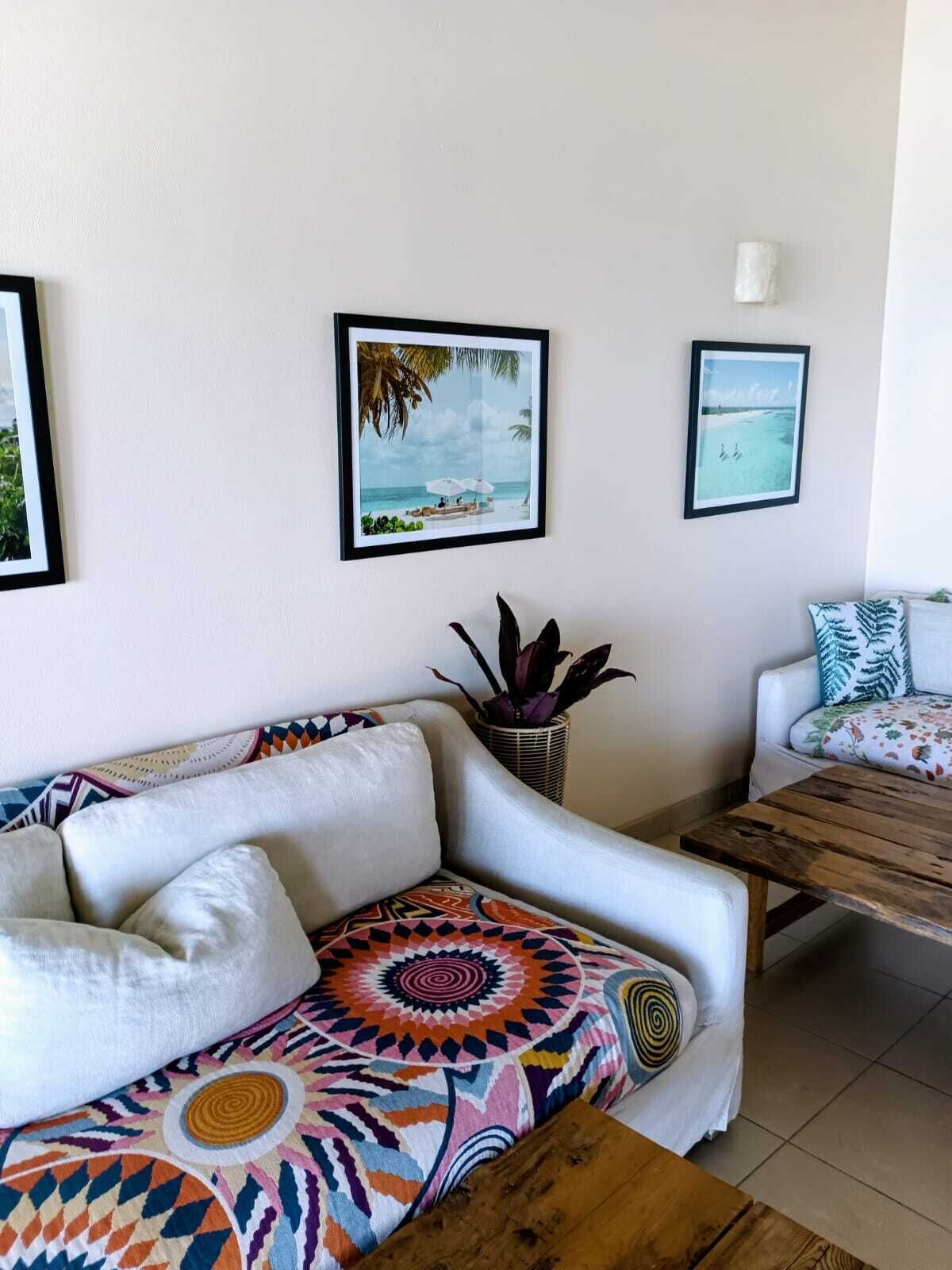 A living room with a white sofa, a colorful patterned throw, a wooden coffee table, and two framed pictures on the wall.