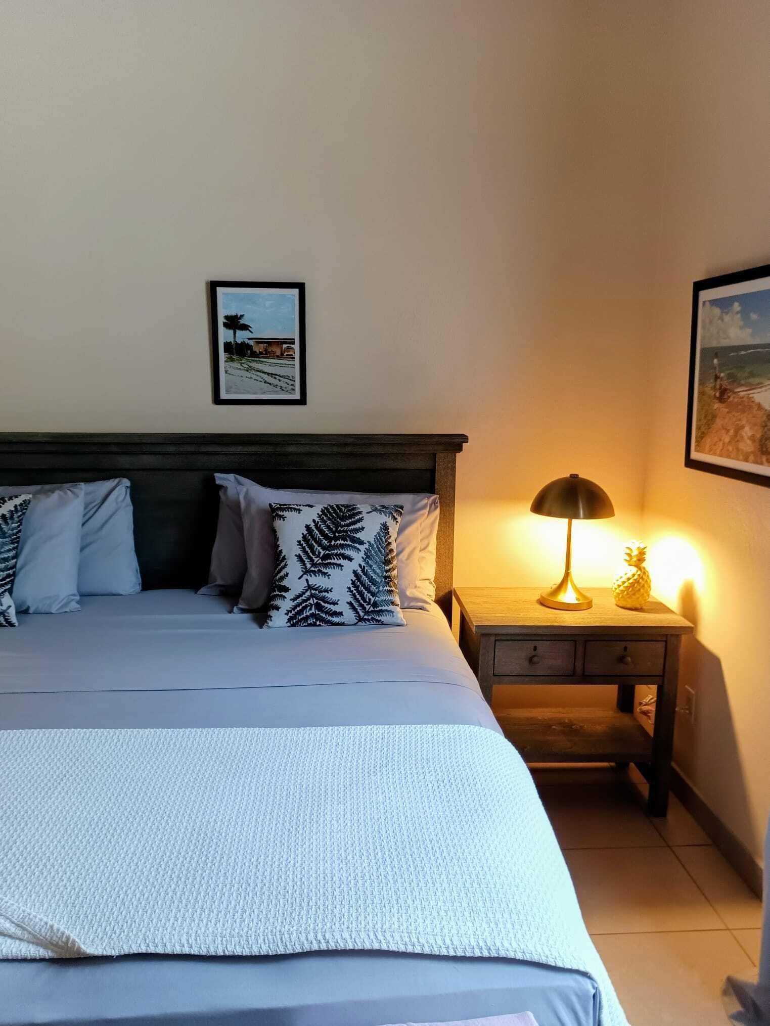A neatly made bed with a patterned pillow, a bedside lamp, and a small wooden nightstand with a picture frame on the wall above.