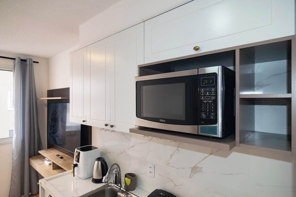 A modern kitchen with white cabinets, a built-in microwave, a coffee maker, and a sink.