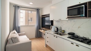 A compact kitchen with white cabinets, a built-in microwave, a stove, and a window with curtains. - Cozy Apartment for 2 (between CGH and Interlagos) (São Paulo)