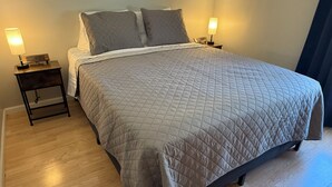 A neatly made bed with a quilted bedspread, two bedside tables with lamps, and a wooden floor.