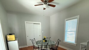 A dining area with a round table, four chairs, a ceiling fan, and a window with blinds.