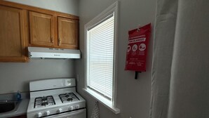 A compact kitchen with wooden cabinets, a white stove, and a window with blinds.