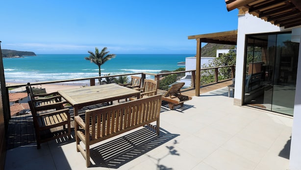 Terraza de madera con mesa y sillas que da a una playa.