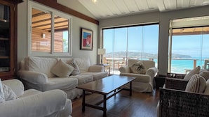 Un salón amplio con sofás blancos, una mesa de centro de madera y grandes ventanales con vistas al océano.