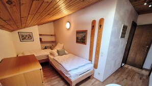 A bedroom with two beds, a wooden ceiling, a large window, a painting, and a bathroom with a bathtub. - Cozy vacation apartment in Reit im Winkl - perfect for your vacation (Reit im Winkl)