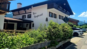 A white building with 'Haus Bergkristall' signage, wooden balconies, and a view of mountains. - Cozy vacation apartment in Reit im Winkl - perfect for your vacation (Reit im Winkl)
