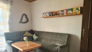 A living room with a grey sofa, a wooden coffee table, a bookshelf with colorful books, and a decorative heart on the wall. - Cozy vacation apartment in Reit im Winkl - perfect for your vacation (Reit im Winkl)