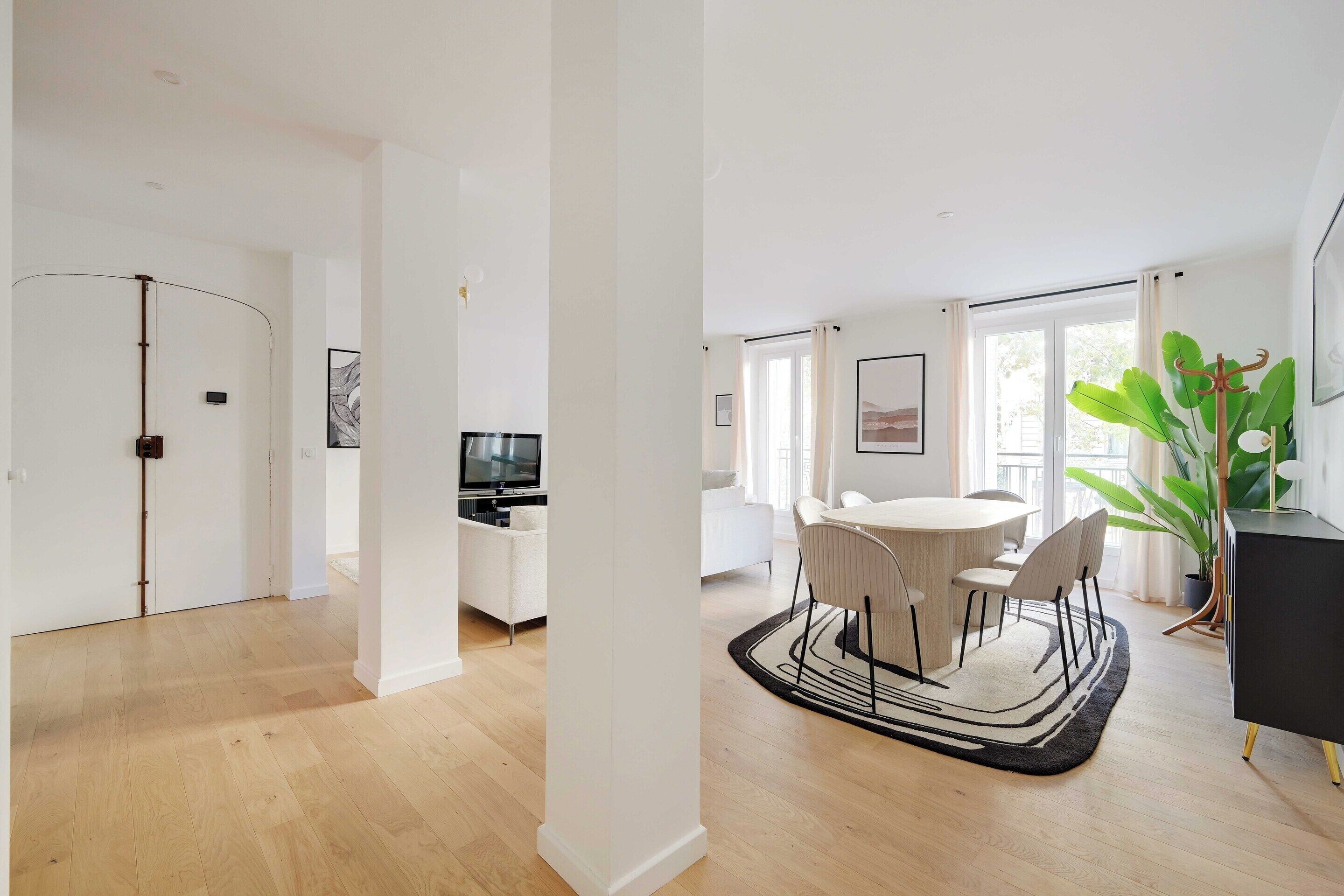 Een ruime woonkamer met een eettafel, stoelen, een televisie en een grote plant.