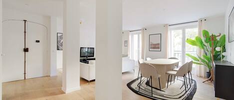 A spacious living area with a dining table, chairs, a TV, and a large plant.