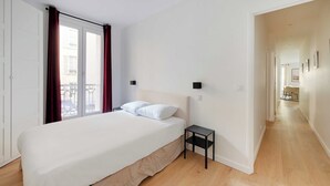 A bedroom with a bed, a nightstand, a window with curtains, and a view of a balcony. - Superb apt A/C - 2br/6p - St Germain-des-pres (Paris)