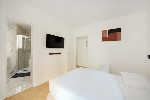 A hotel room with a bed, a television mounted on the wall, a shower with marble walls, and a door leading to another room. - Superb apt A/C - 2br/6p - St Germain-des-pres (Paris)