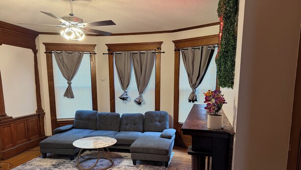 Ein Wohnzimmer mit Ecksofa, Couchtisch, Deckenventilator und Kamin mit Pflanze.