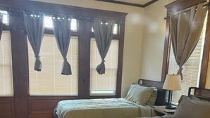 Ein Schlafzimmer mit zwei Betten, einem gemusterten Teppich, Holzboden und großen Fenstern mit Vorhängen.