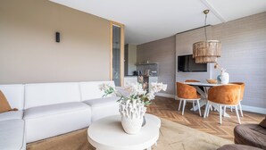 A modern living room with a white sofa, a round coffee table with a white vase, and a dining area with orange chairs and a wooden table. - Inviting Apartment With a Garden (Sint Maartensvlotbrug)