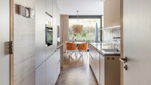 A modern kitchen with a herringbone wood floor, white cabinetry, and a dining area with two orange chairs. - Inviting Apartment With a Garden (Sint Maartensvlotbrug)