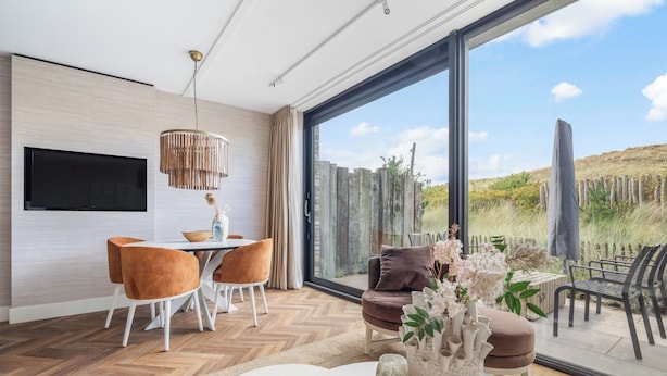 A modern living room with a large TV, dining area, and a view of a garden through large windows. - Inviting Apartment With a Garden (Sint Maartensvlotbrug)