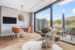 Una sala de estar moderna con un televisor grande, comedor y vistas a un jardín a través de amplios ventanales.