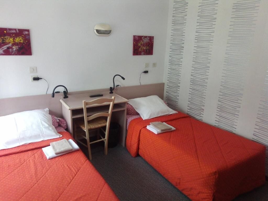 Ein Hotelzimmer mit zwei Einzelbetten, einem Schreibtisch mit Stuhl, einer Wandleuchte und zwei Bildern.