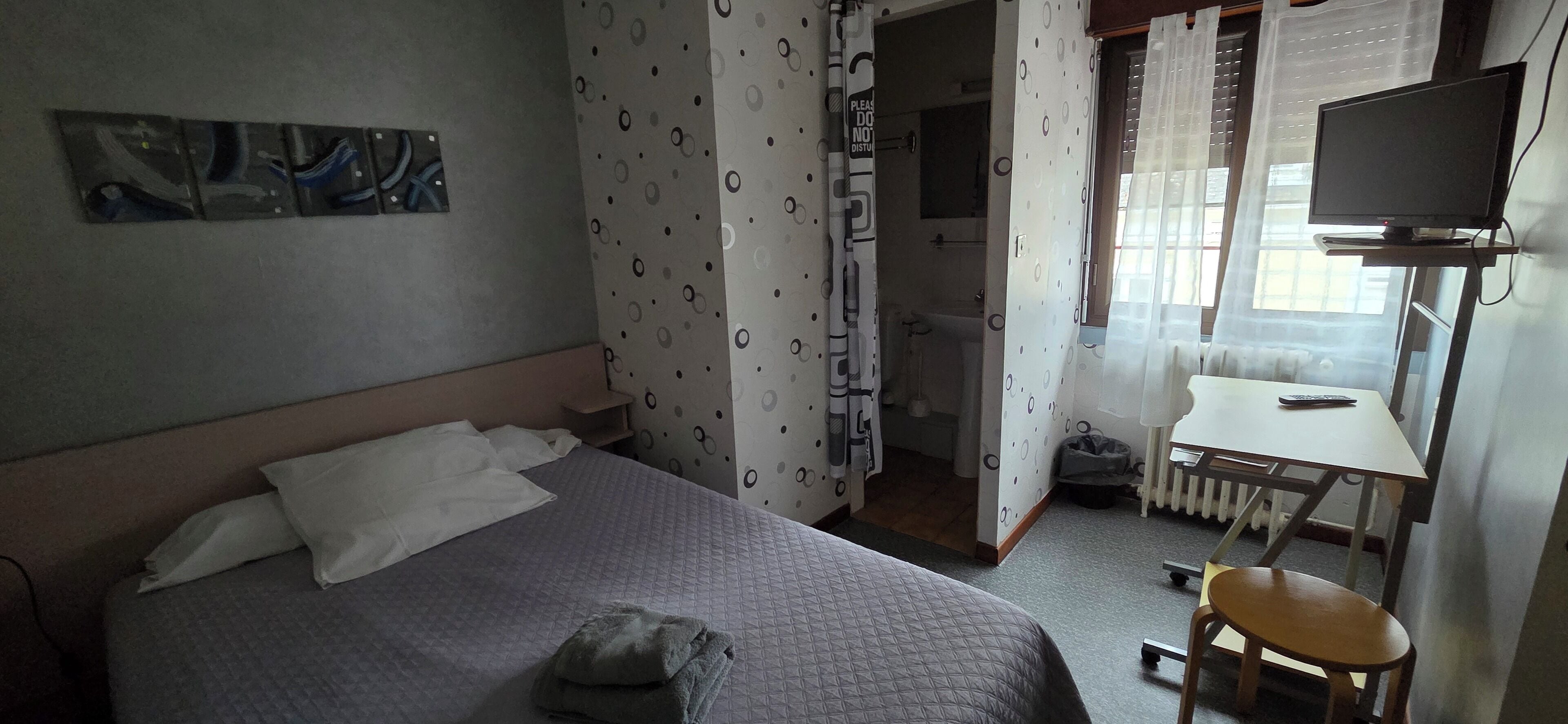 Quarto de hotel com cama, escrivaninha e cadeira, televisão e banheiro visível por uma porta aberta.