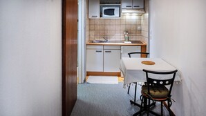 A compact kitchen with a microwave, sink, and cabinets. There's a dining table with a chair and a rug on the floor. - Hotel des Touristes (Pierrefitte-Nestalas)