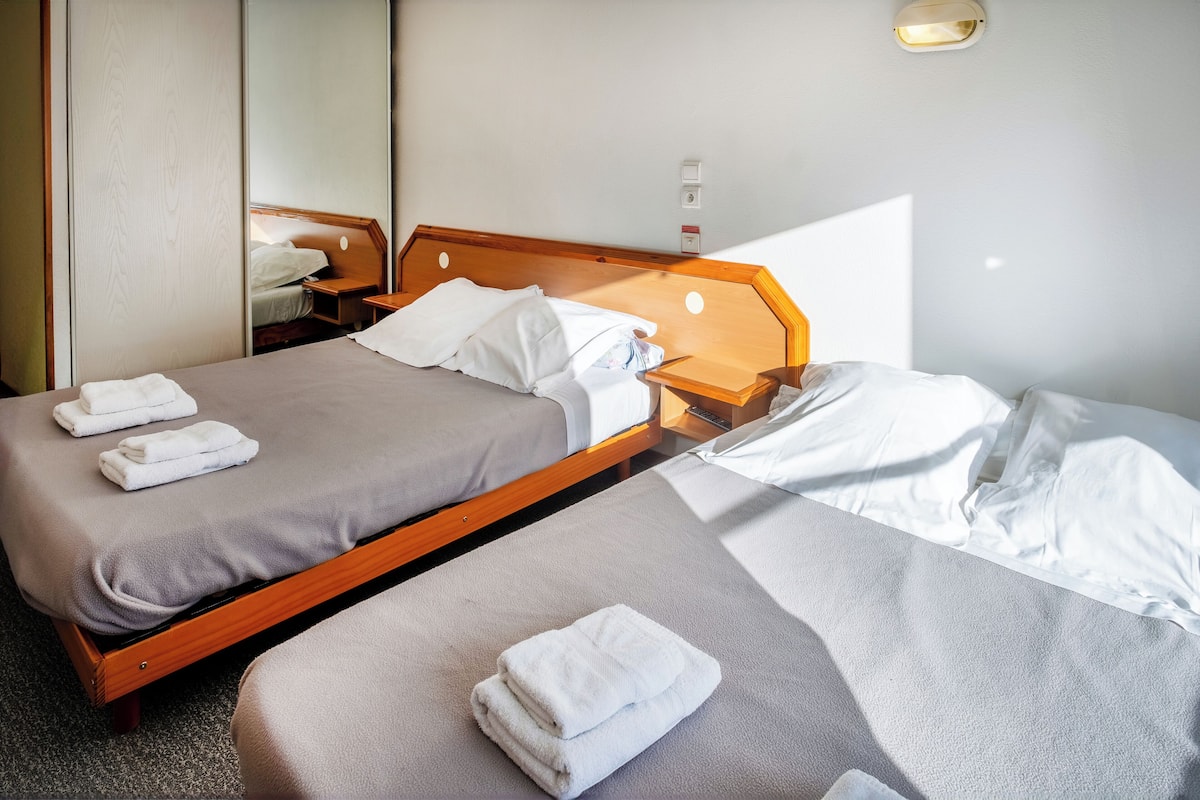A hotel room with two beds, each with a wooden headboard, and a small bedside table with a lamp.