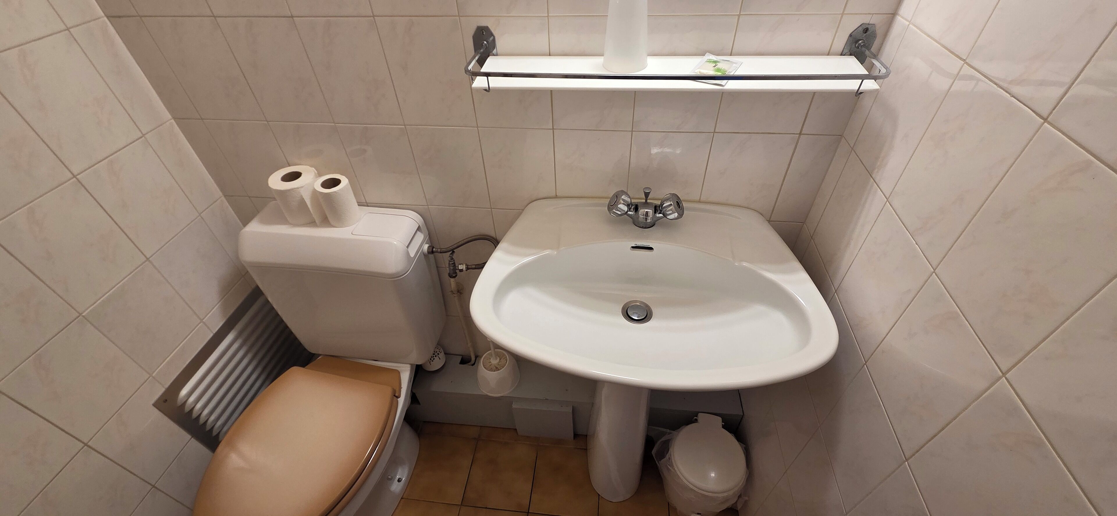Un baño pequeño con inodoro, lavamanos y repisa sobre él.