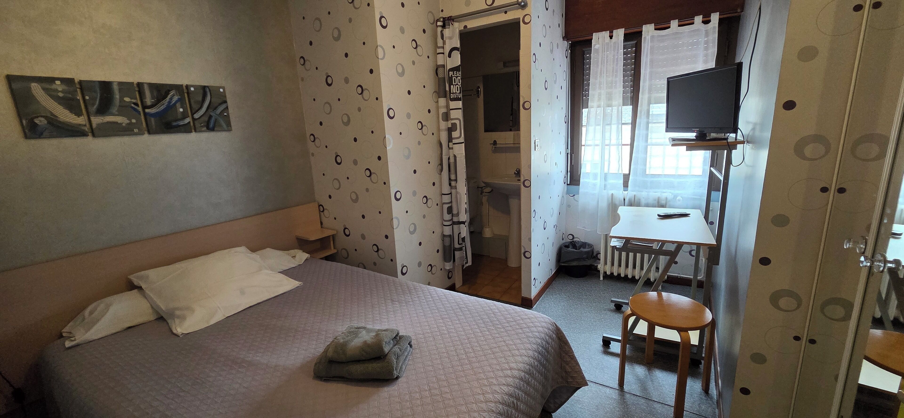 A hotel room with a bed, a desk, a chair, and a TV.