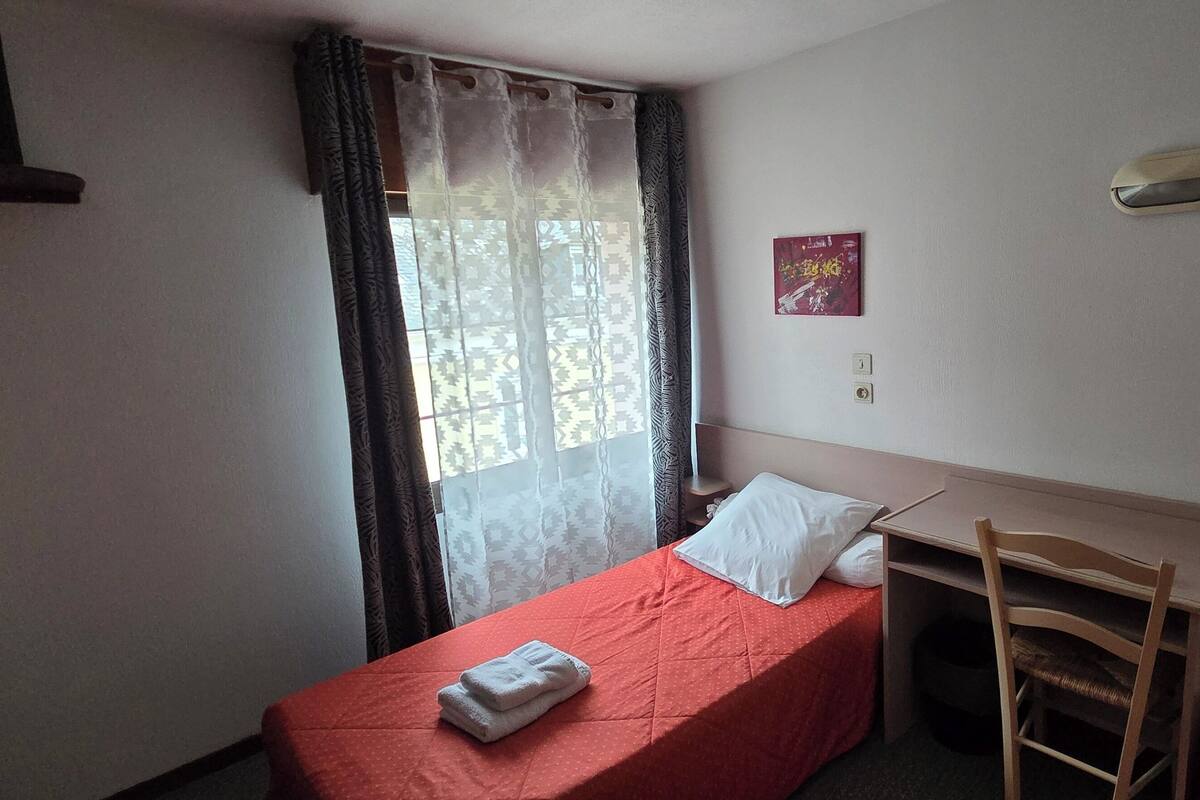 A small, neatly arranged room with a single bed, a desk, and a chair.