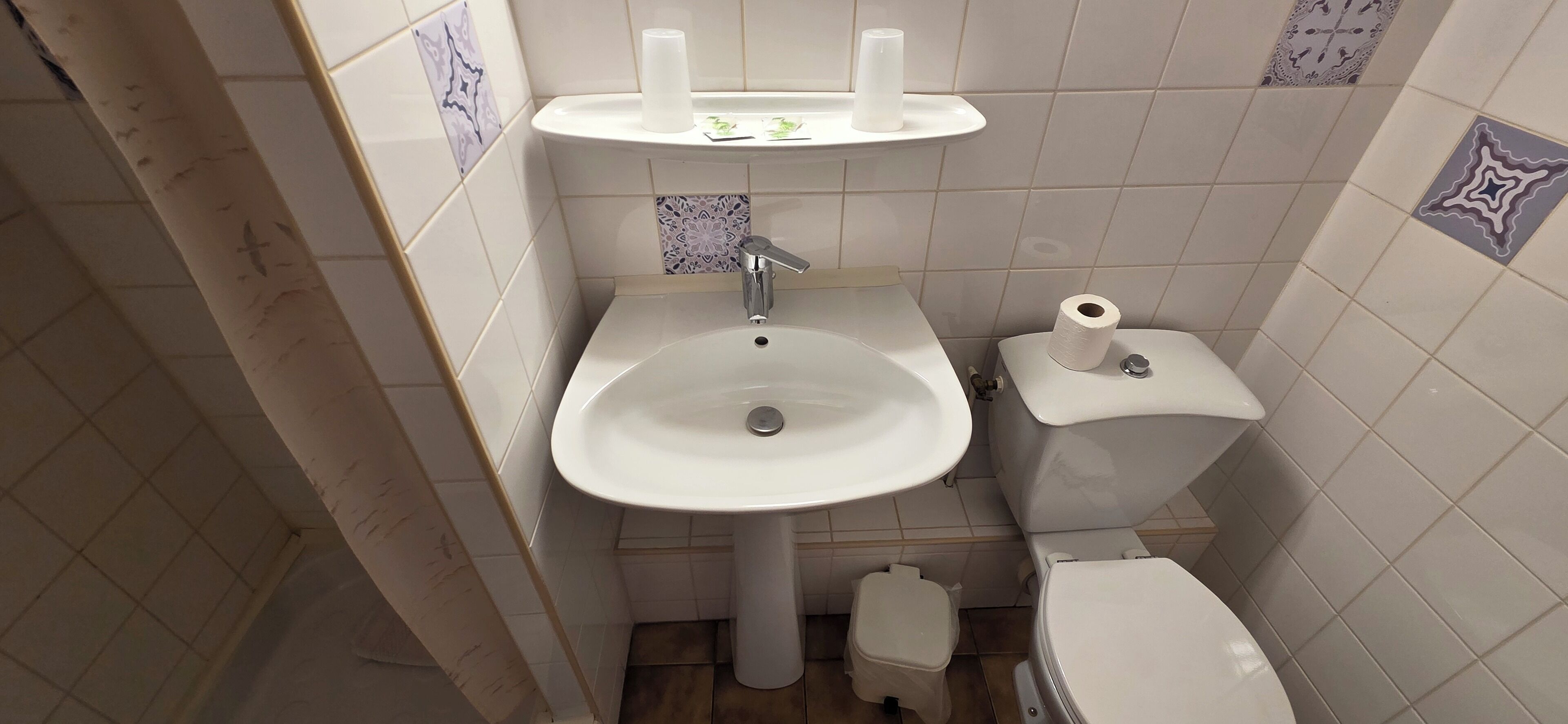 Un baño con lavamanos blanco, inodoro y un pequeño cubo de basura.