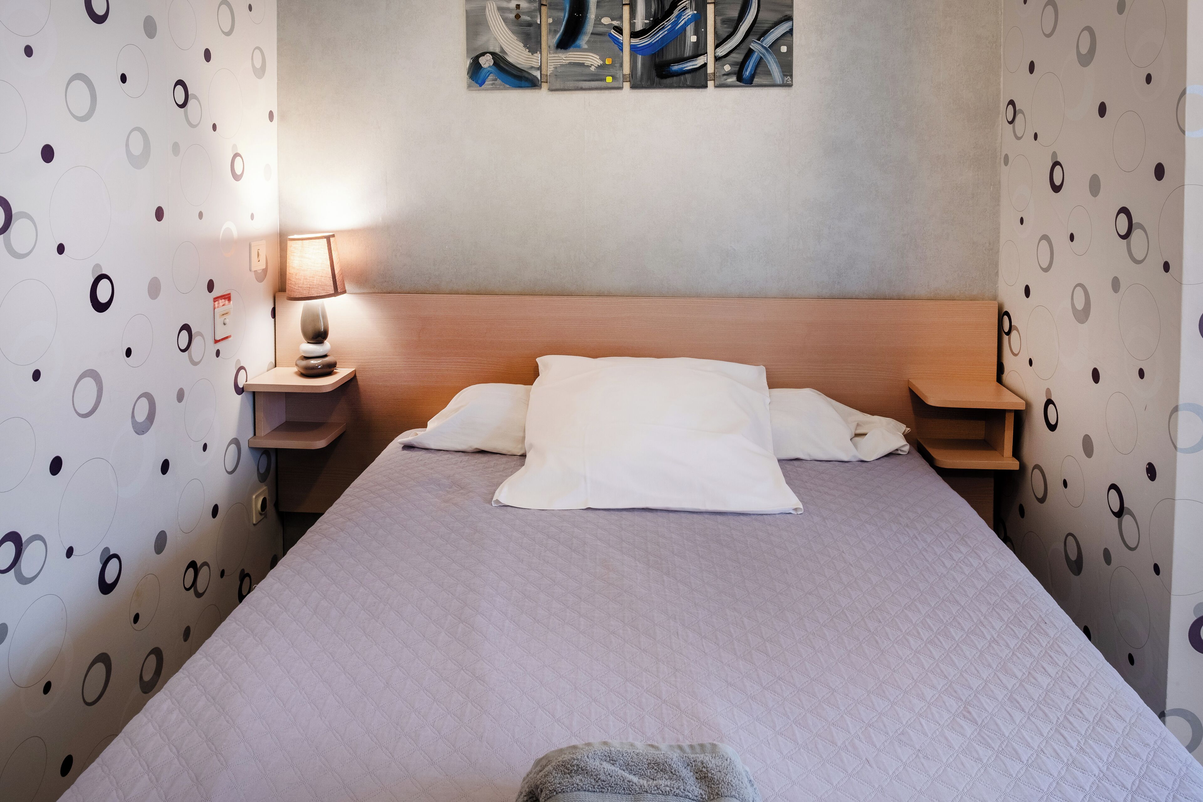 A neatly made bed with white bedding, a wooden headboard, and a bedside table with a lamp.