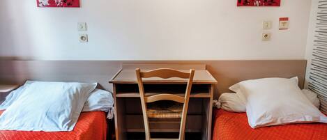 A hotel room with two single beds, a wooden desk, and two paintings on the walls.