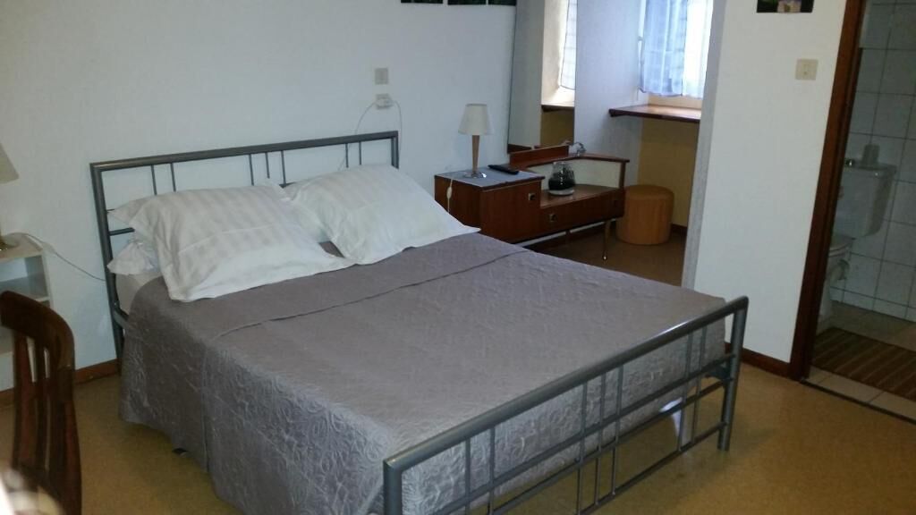 Een slaapkamer met een bed met metalen frame, een houten nachtkastje, een lamp en een kleine tafel.