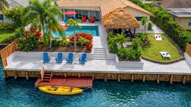 A resort with a pool, a thatched-roof structure, and a dock with a boat. - Waterfront w/ Htd Pool, Tiki Hut, Billards, & Bar (Boynton Beach)